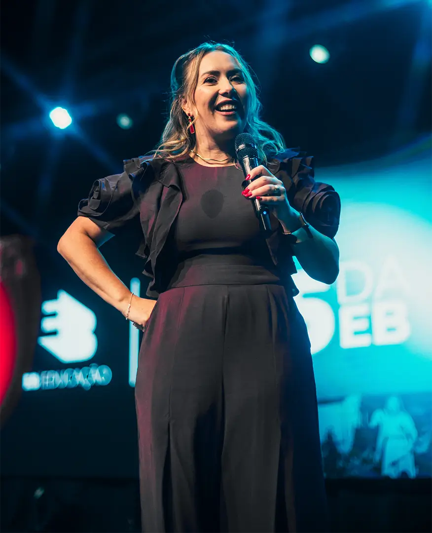 Euza Bispo no palco, com microfone na mão, durante um evento da EB Educação.